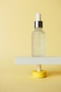 Serum facial moisturizer bottle standing on abstract pedestal on pastel yellow background with copy space, front view. Blank glass