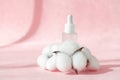 Serum oil with collagen and peptide in white transparent bottle with dropper on pink decor backdrop with cotton flowers