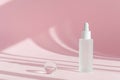 Serum oil with collagen and peptide in white transparent bottle with dropper on pink decor backdrop with shadows