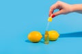 Serum in a transparent bottle with a pipette hold hand with yellow lemons on blue background. Royalty Free Stock Photo