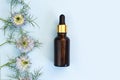Serum in unbranded brown glass bottle with pipette, line frame border of blue Nigella flowers on blue background. Cosmetic bottle