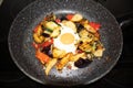Serve one fried egg with baked vegetables, sausage. Round bright yellow yolk in the center