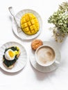 Served breakfast - cappuccino, fresh ripe mango, spinach sandwich with boiled egg on a light background, top view