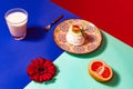 Served table. Food pop art photography. Glass of milk, cake and flower on blue and turquoise color tablecloth over red