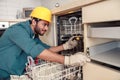 Focused handyman in special clothing repairing dishwasher in modern kitchen Royalty Free Stock Photo