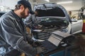 Serviceman making car diagnostics with a laptop in a workshop , his colleague working in the background