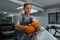 Serviceman polishing car body part in workshop