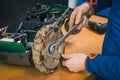 Serviceman stripping and removing wheels on robotic lawnmower, motorized lawnmower being serviced on a table after a year of use