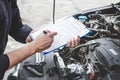 Services car engine machine concept, Automobile mechanic repairman checking a car engine with inspecting writing to the clipboard