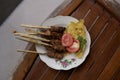 A serving of Balinese fish satay topped with fresh tomatoes, celery and crispy chips, placed on a vintage wooden table. Looks