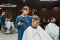 Serving client in barbershop. Professional young barber girl drying hair of a handsome guy, making trendy haircut. Focus Royalty Free Stock Photo