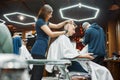 Serving client in barbershop. Side view of a professional young barber girl making trendy haircut for a young guy Royalty Free Stock Photo