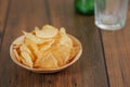 Serving of fresh crisps in wooden small bowl and empty glass and bottle of lager beer in the background on a brown wooden table Royalty Free Stock Photo