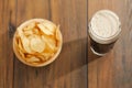 Serving of fresh crisps in wooden small bowl and a pint glass with dark stout beer with white foam on top on a dark wood table Royalty Free Stock Photo