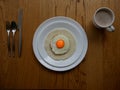 Serving of a fried egg with orange yolk over a corn cake served for serving breakfast on a white round plate over a wood Surface