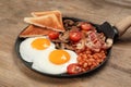 Serving pan with fried eggs, mushrooms, beans, bacon, tomatoes and toasted bread on wooden table, closeup. Traditional English Royalty Free Stock Photo