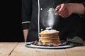 Serving pancakes with powdered sugar and berries. Chef man hand. Beautiful food still life. slightly toned image, dark black backg