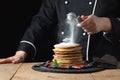 Serving pancakes with powdered sugar and berries. Chef woman hand. Beautiful food still life. slightly toned image, dark black bac