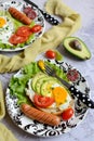 Serving plate with appetizing scrambled eggs, tomatoes, avocado and sausages on a gray background. Vertical, close-up Royalty Free Stock Photo