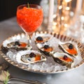 Serving tray with oysters on crushed ice staffed with red and black caviar and a glass of red caviar. Texture of red caviar.