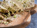 Sesame halva with pistachios on a teak chopping board on a grey background.