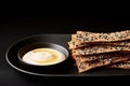Sesame seed crackers with creamy dip on black plate against dark background Royalty Free Stock Photo