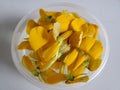 Sesbania flowers float on water in clear plastic bowl with white marble background.