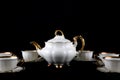 Set of antique porcelain cups and teapot with gilding on a black background.