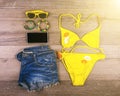 Set of beach clothes yellow bikini, bracelets, jeans shorts, glasses on dark wooden background. Top view. Summer Holiday Royalty Free Stock Photo