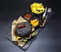 Set of the black burger. Stone plate with: black burger roll slices of juicy marble beef, fused cheese, fresh salad with French fr Royalty Free Stock Photo