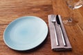 Set of blue empty plate, napkin, fork and knife on brown wooden table in restaurant Royalty Free Stock Photo