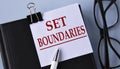 SET BOUNDARIES - words on a white piece of paper on a black notebook with a pen and glasses