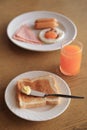 Set of breakfast, toast with butter and orange juice, and plate of fried egg, ham, sausage on background