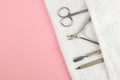 A set of cosmetic tools for manicure and pedicure. Manicure scissors, cuticles, saws on white towel stand on a pink background.