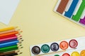 A set for creativity and drawing: watercolor paints, plasticine and multicolored pencils on a yellow background. Top view