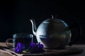 Set of Cup and metal pot of Butterfly pea tea with frehh violet flower on brown tablecloth and wwoden table on black background. Royalty Free Stock Photo