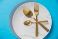 Set of cutlery spoon, fork, plate, isolated on blue background. White marble plate. Top view .Table setting with gold Royalty Free Stock Photo