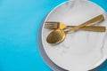 Set of cutlery spoon, fork, plate, isolated on blue background. White marble plate. Top view .Table setting with gold Royalty Free Stock Photo