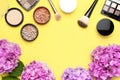 Set of decorative cosmetics mascara powder lipstick eyeshadow blush makeup brush pink hydrangea flowers on yellow background top Royalty Free Stock Photo