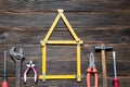 Set of different work tools are in the form of a house: screwdriver, hammer, hand saw, meter, wrench over dark wooden background.