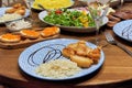 A set dinner table with various dishes and salads, in the foreground a plate of rice and fried fish Royalty Free Stock Photo