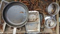 A set of dirty pots pans trays and utensils in a mud kitchen outdoors