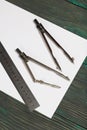 Set for drawing. Two compasses, a metal ruler and a sheet of white paper. They lie on pine boards painted in black and green Royalty Free Stock Photo