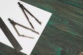 Set for drawing. Two compasses, a metal ruler and a sheet of white paper. They lie on pine boards painted in black and green Royalty Free Stock Photo