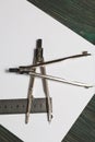 Set for drawing. Two compasses, a metal ruler and a sheet of white paper. They lie on pine boards painted in black and green