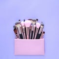 Set of essential professional make-up brushes and cosmetic bag on pastel purple background