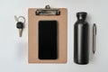Common office desk items arranged neatly with a clipboard, smartphone, water bottle, pen, and keys Royalty Free Stock Photo