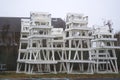 Collection of stored lifeguard chairs, on yellowed grass with leafless hedge and house in background