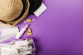 Set for flight small bottles with cosmetics, hat, earplugs, nasal spray, air ticket and documents on purple background. Top view,