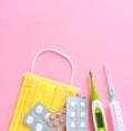 Pills, capsules, thermometer, surgical mask on the bright pink background